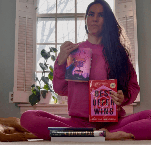 The blog author sitting in a pink outfit, holding up two books that are also pink.